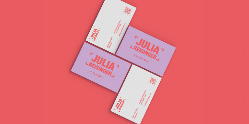 Visitenkarten-Design für die Fotografin Julia Reisinger. Die Karten präsentieren ein auffälliges Branding mit kräftigen Farben in Rot und Lila. Der Name und das Logo sind groß und zentral platziert, mit dem Zusatz 'Fotografie' darunter. Eine saubere, minimalistische Gestaltung sorgt für eine moderne und professionelle Wirkung. Die Rückseite der Visitenkarten enthält Kontaktinformationen und einen QR-Code. Das Design unterstreicht die kreative und zeitgemäße Identität der Fotografin.